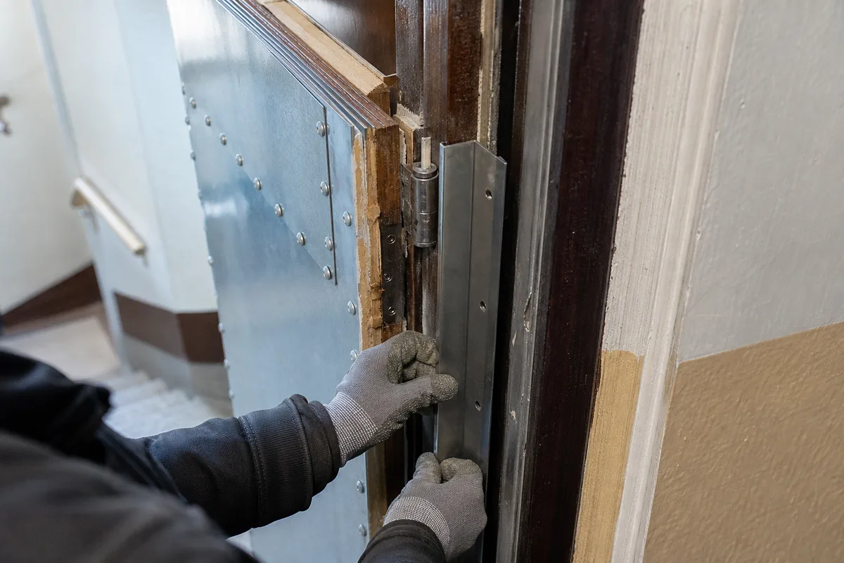 Tôle d&rsquo;acier et cornière anti-pince posées sur un bloc-porte en bois massif d&rsquo;immeuble ancien