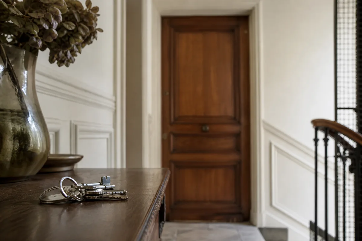 Palier d&rsquo;immeuble ancien avec une porte en bois massif refermée et un trousseau de clés resté à l&rsquo;intérieur